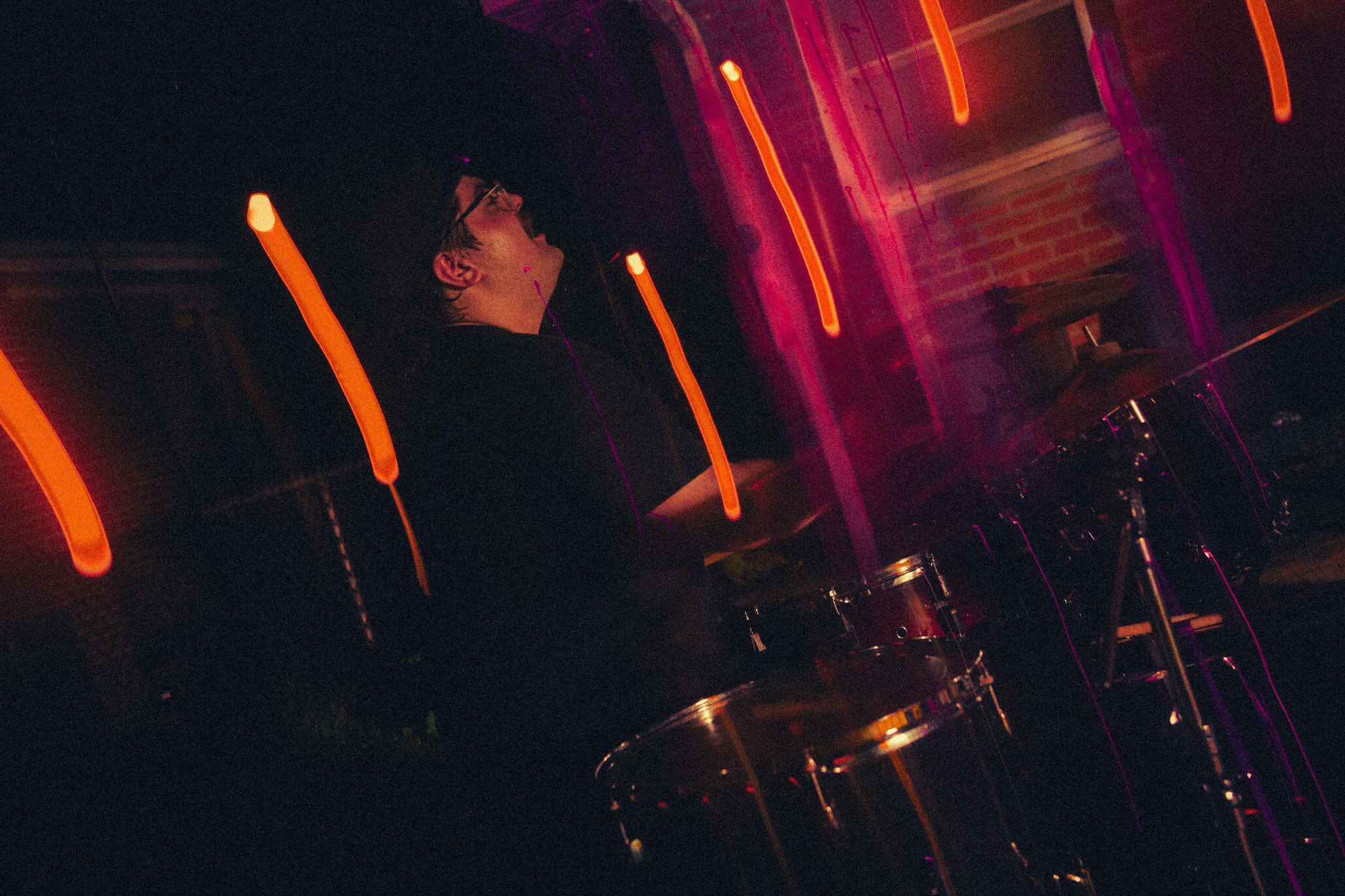 Drummer performing under orange and magenta lights